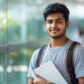 A student smiles while holding a notebook, embracing the vibrant campus atmosphere around him.